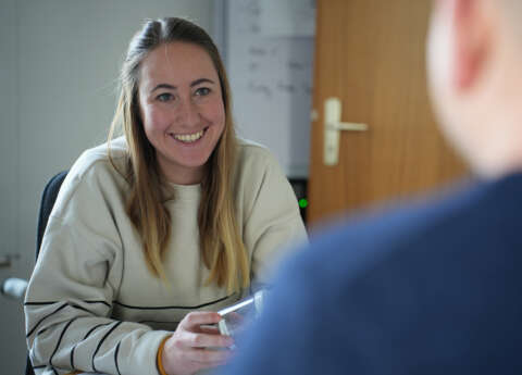 Eine Frau sitzt an einem Tisch und lächelt einen Mann an.
